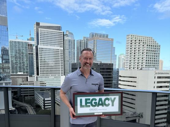  Tim Holt holds the Legacy Award with the backdrop of a city behind him 